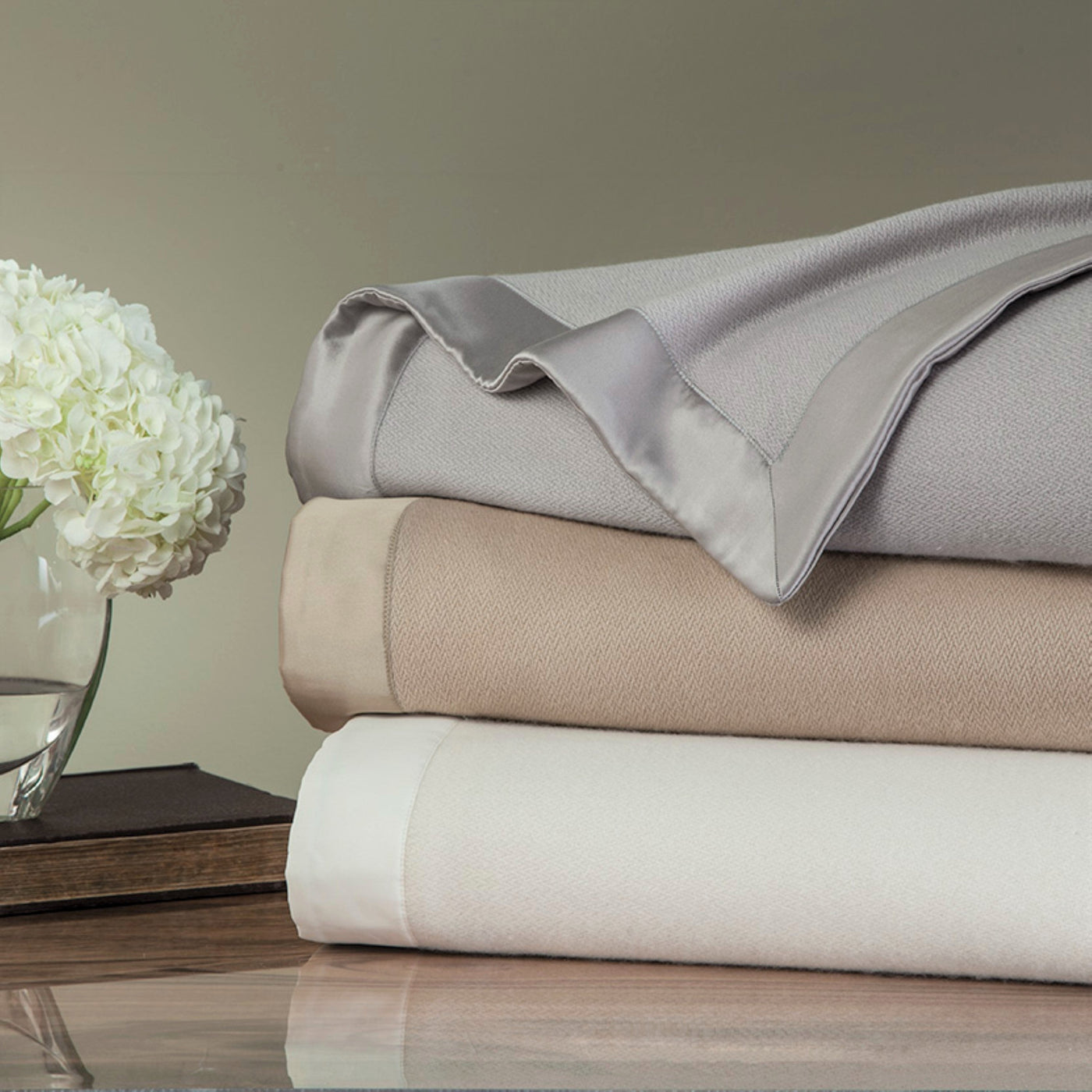 Home Treasures Serena blankets stacked in silver, champagne, and ivory with satin trim.