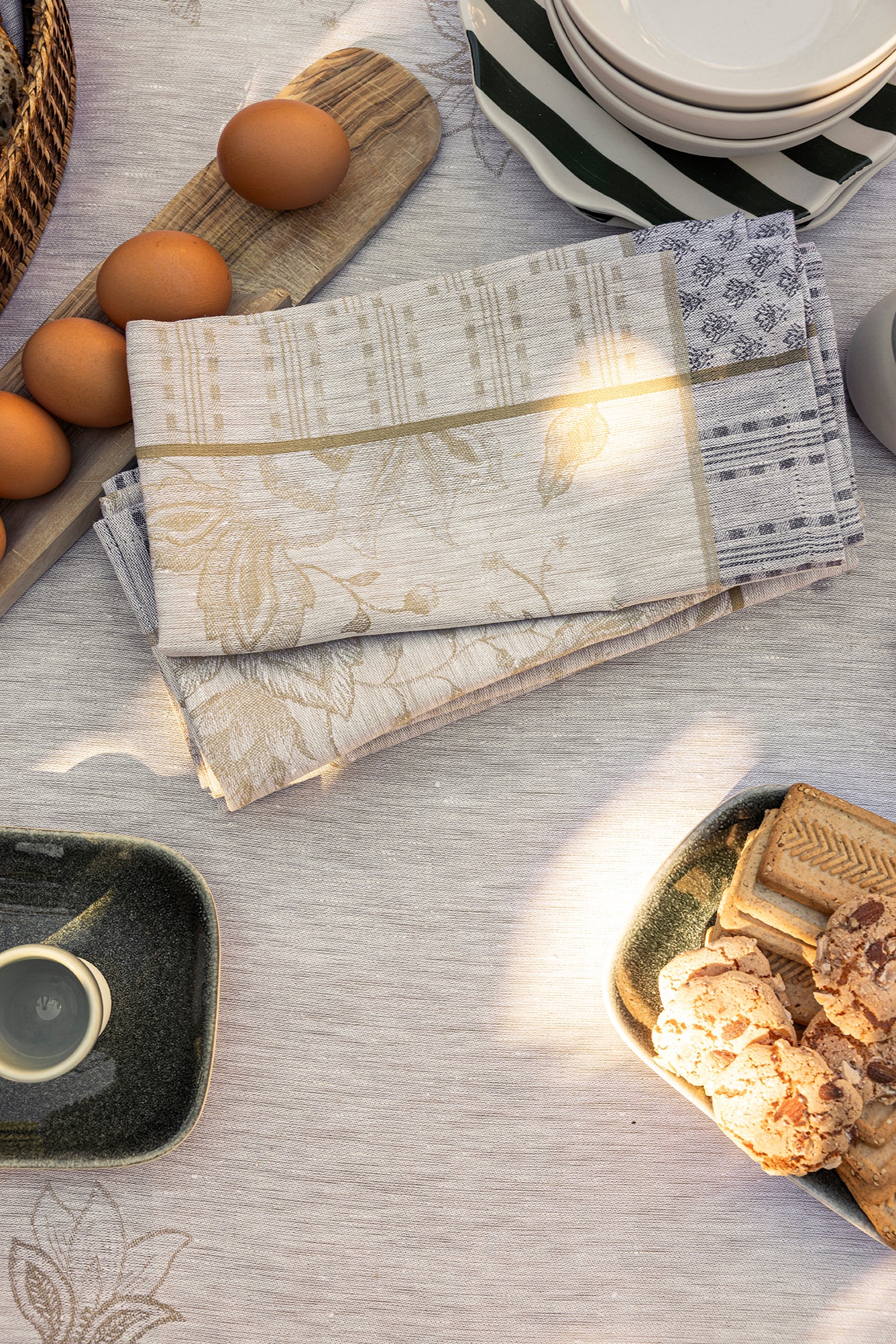Folded champagne and gold jacquard napkins with floral motif, styled on a linen table with eggs and ceramics.