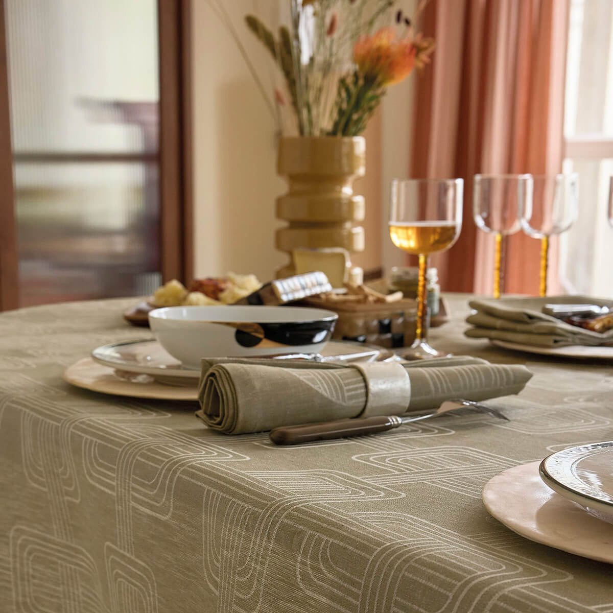 Close-up of green Le Jacquard Français napkin rolled with silverware on a geometric jacquard tablecloth.