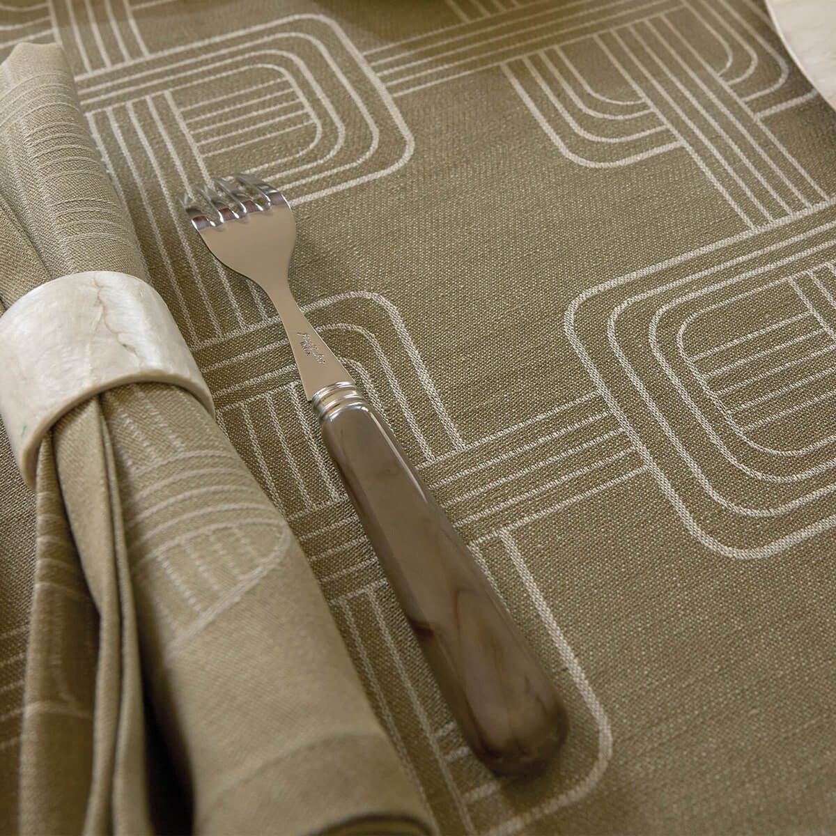 Close-up of Green Le Jacquard Français dinner napkin with geometric Art Deco pattern, styled with fork and napkin ring.