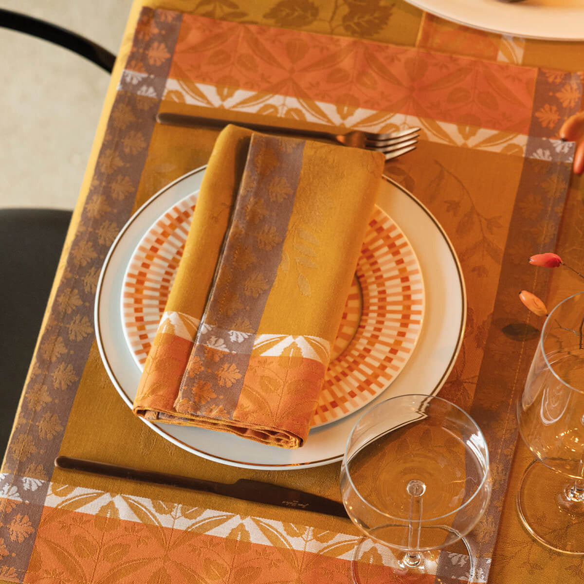 Le Jacquard Français Manor Lane napkin folded on plate, Orange floral-border jacquard with placemat setting.