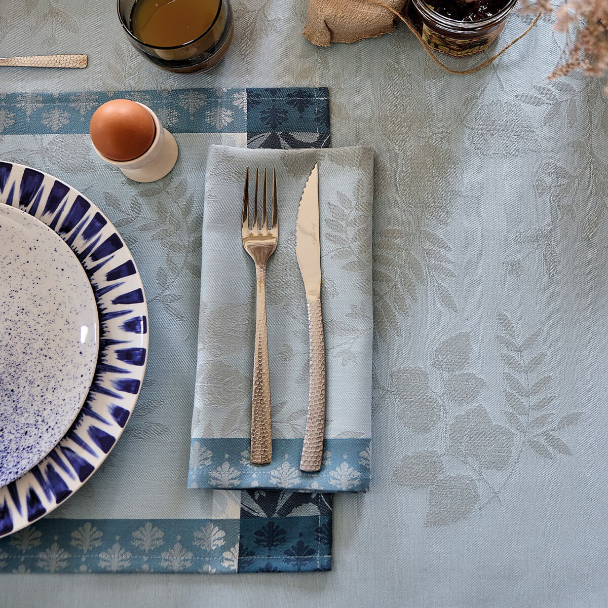Le Jacquard Français Manor Lane dinner napkin in Blue with fork and knife, styled on matching placemat.