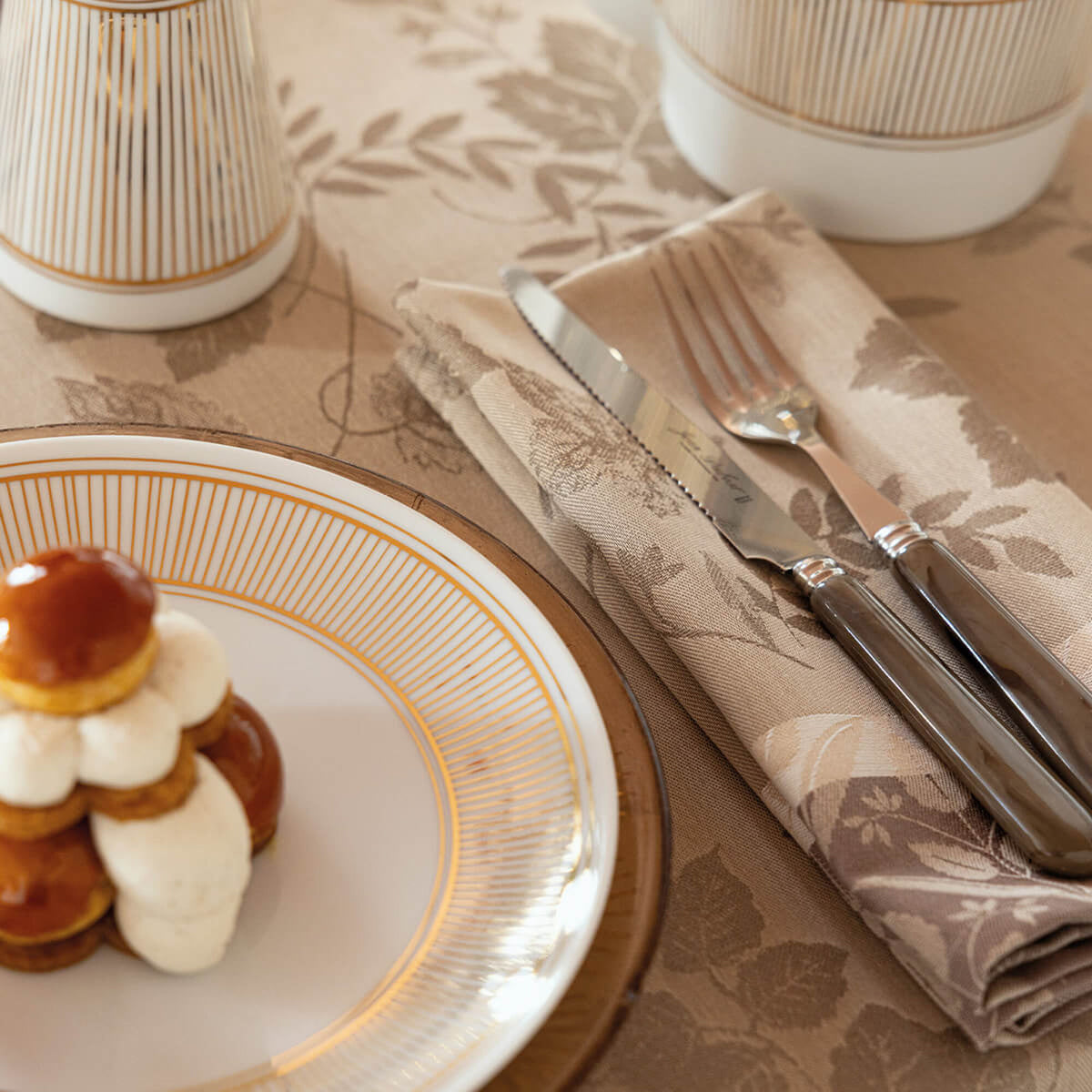 Close-up of Beige Le Jacquard Français Manor Lane napkin with leaf jacquard, folded with silverware.