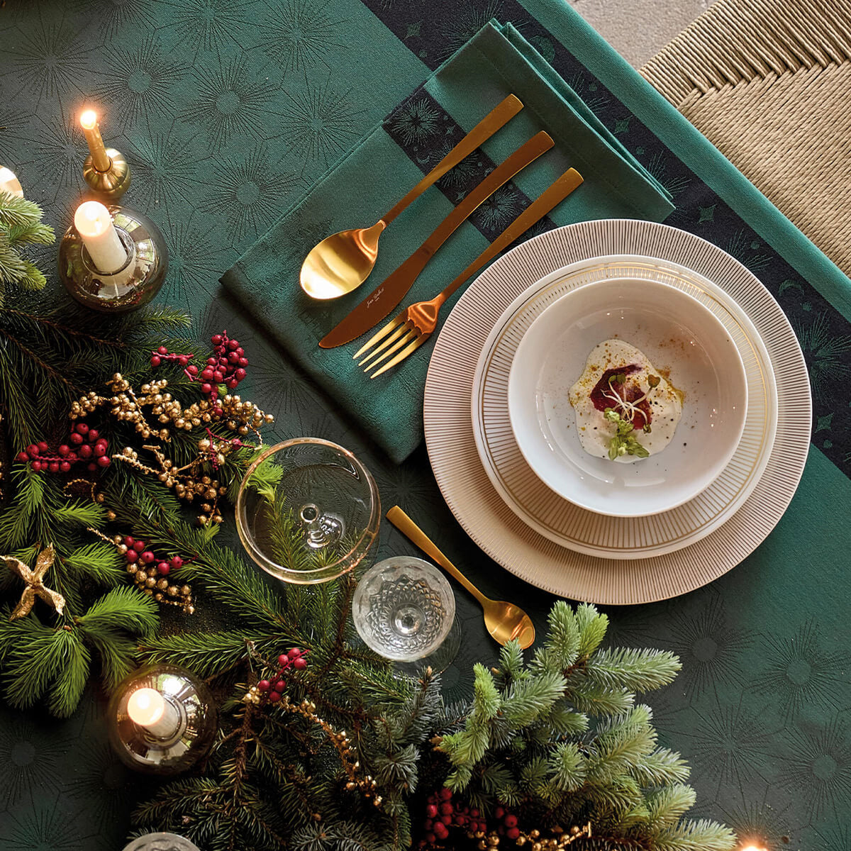 Green Sous les Étoiles napkin folded beneath gold cutlery in a festive Christmas table setting.