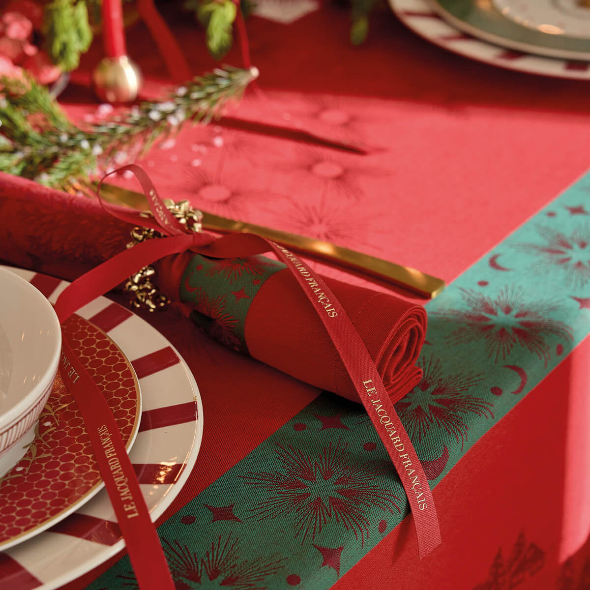 Red and teal Sous les Étoiles napkins rolled with gold ribbon on a festive holiday table setting.