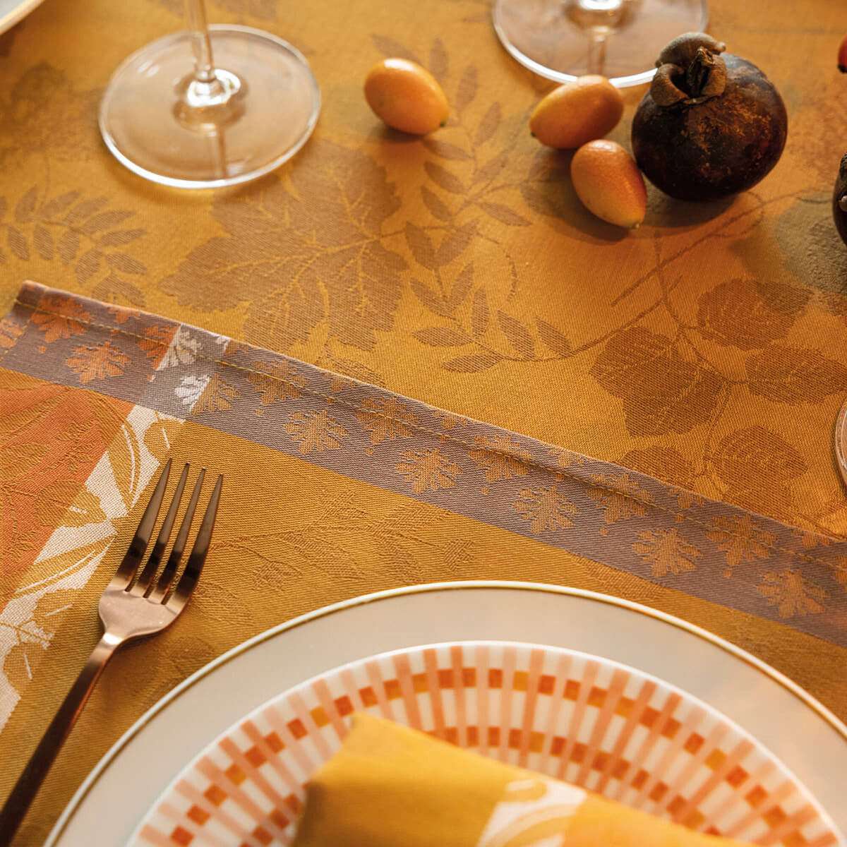 Styled place setting on Orange Manor Lane jacquard tablecloth with leaf motif, fork, and layered plates.