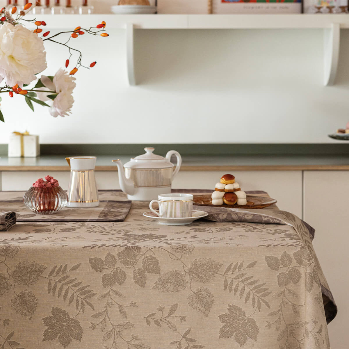 Beige Manor Lane placemats styled on a dining table with teacup, teapot, and floral arrangement.