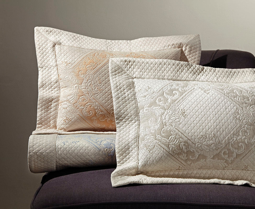 Ivory and champagne quilted pillow shams with baroque embroidery, stacked on a charcoal bed.
