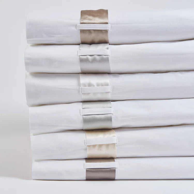 Stack of six Ann Gish Silk Band sheet sets in white with varied satin band colors.