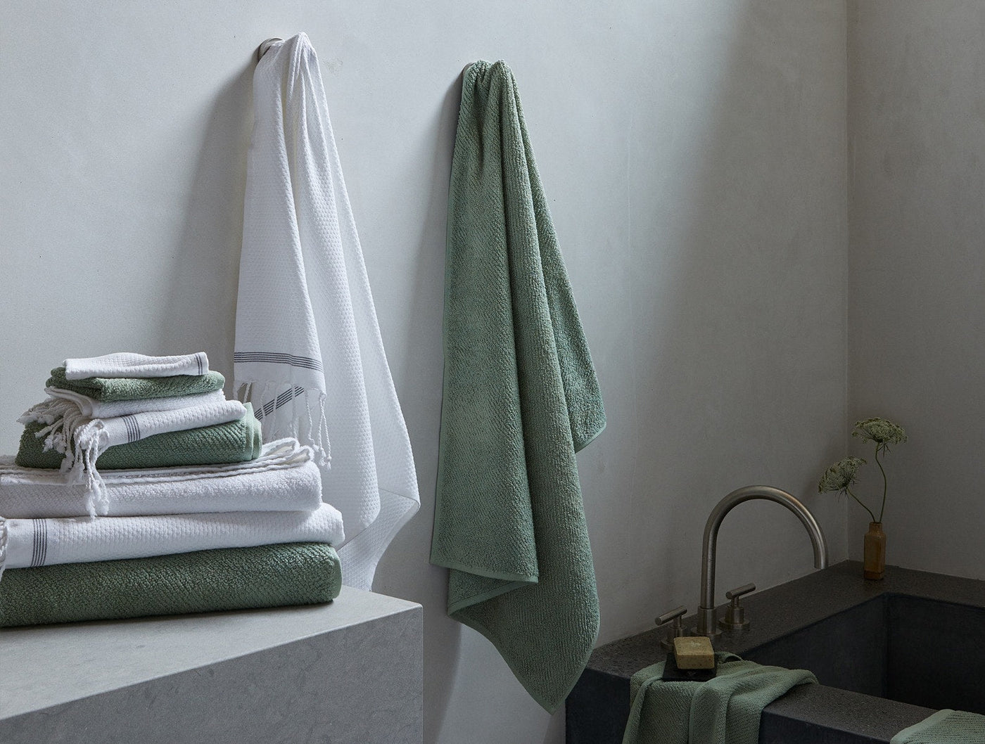 Close-up of Coyuchi Air Weight bath sheets in white and sage green styled in a minimal bathroom.