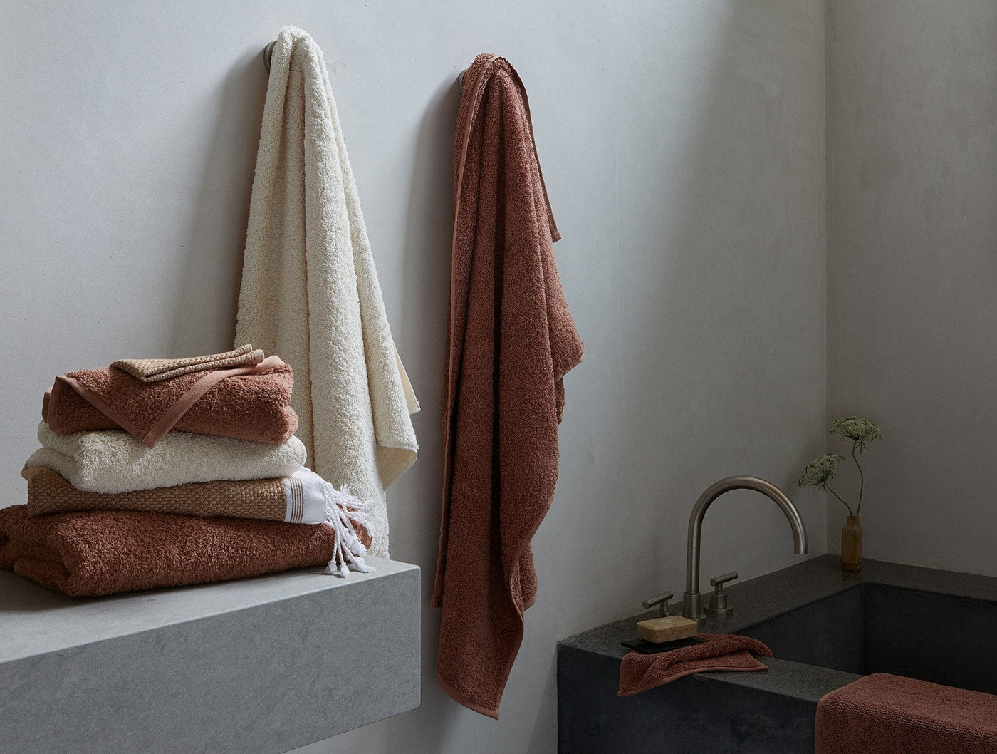 Coyuchi Cloud Loom towels stacked and hung in terracotta and undyed in a minimal bathroom.