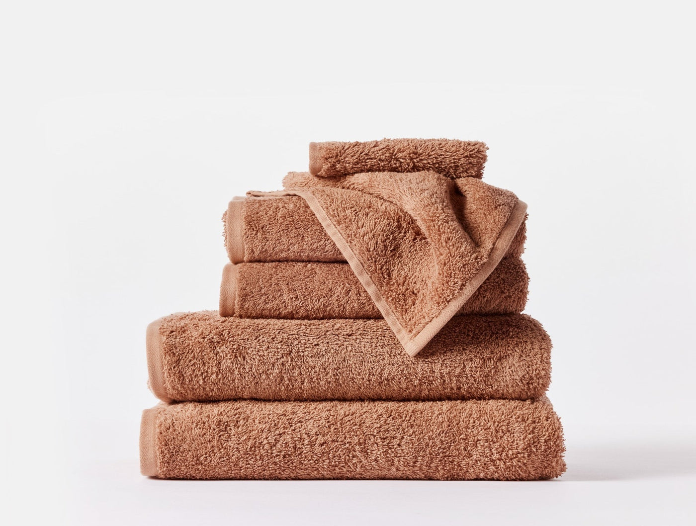 Stacked Coyuchi Cloud Loom towels in warm terracotta, showing varied sizes and looped terry texture.
