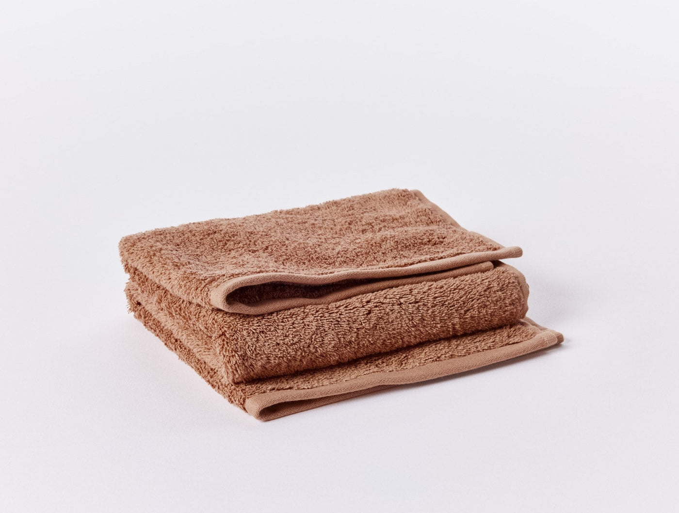 Folded terracotta bath sheet showing plush cloud-loom texture and neatly finished hem edge.