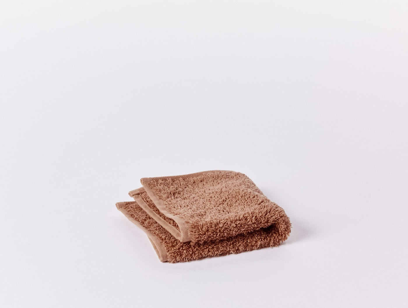 Folded terracotta Coyuchi Cloud Loom washcloth showing dense looped terry texture.