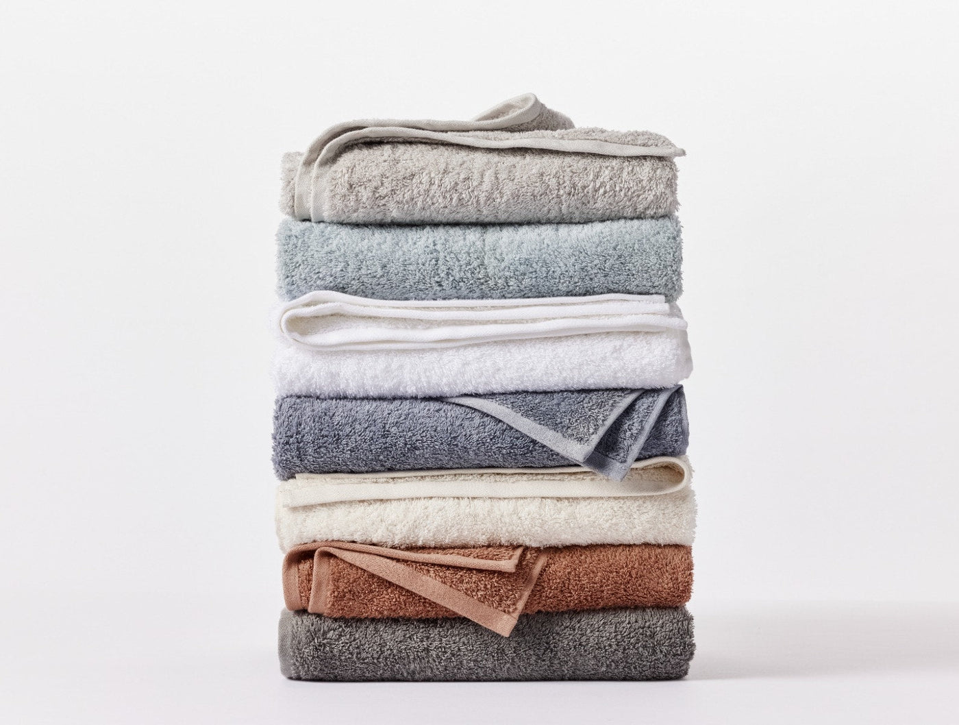 Stack of folded Coyuchi Cloud Loom towels in assorted colors including slate, rust, and ivory.