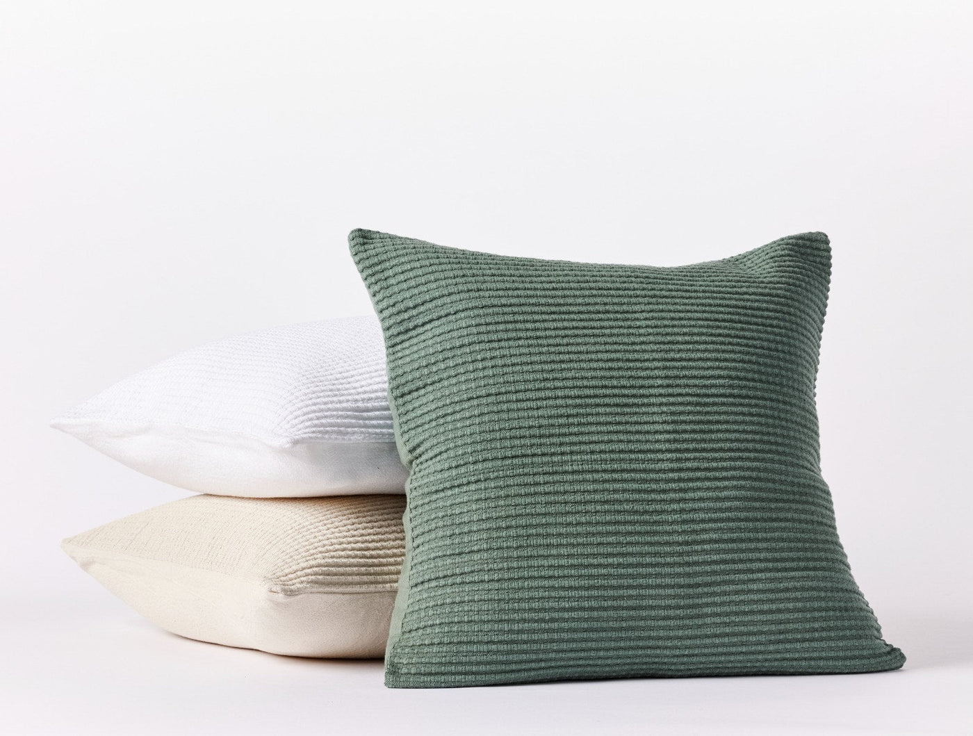 Three Coyuchi Marshall pillows stacked in sage, natural, and white with ribbed texture.