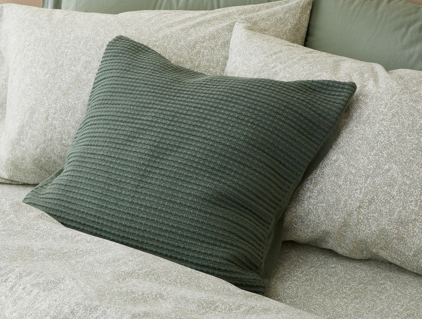 Dark sage green quilted pillow cover styled on a bed with floral bedding.