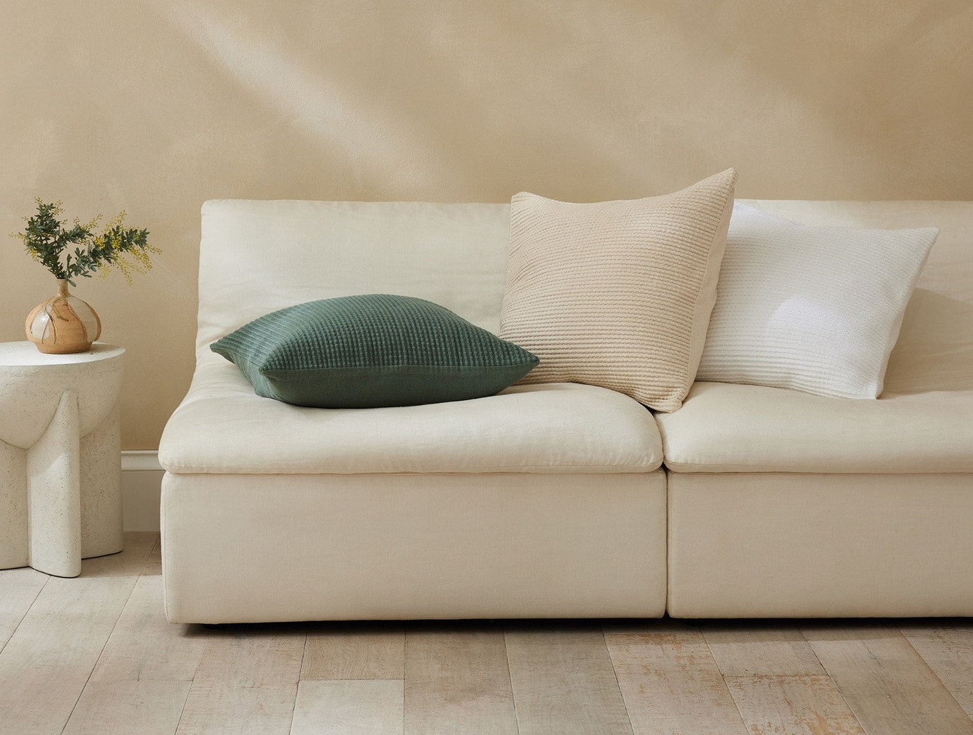 Dark green textured Coyuchi Marshall pillow styled on a cream sofa with neutral cushions.