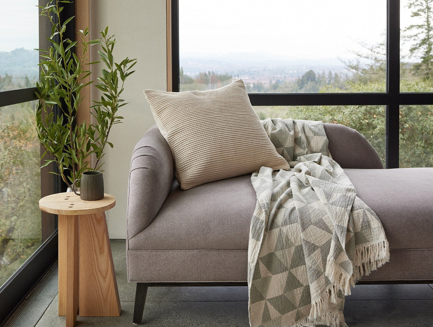 Coyuchi Marshall pillow styled on a chaise lounge beside a draped throw, forest view beyond.