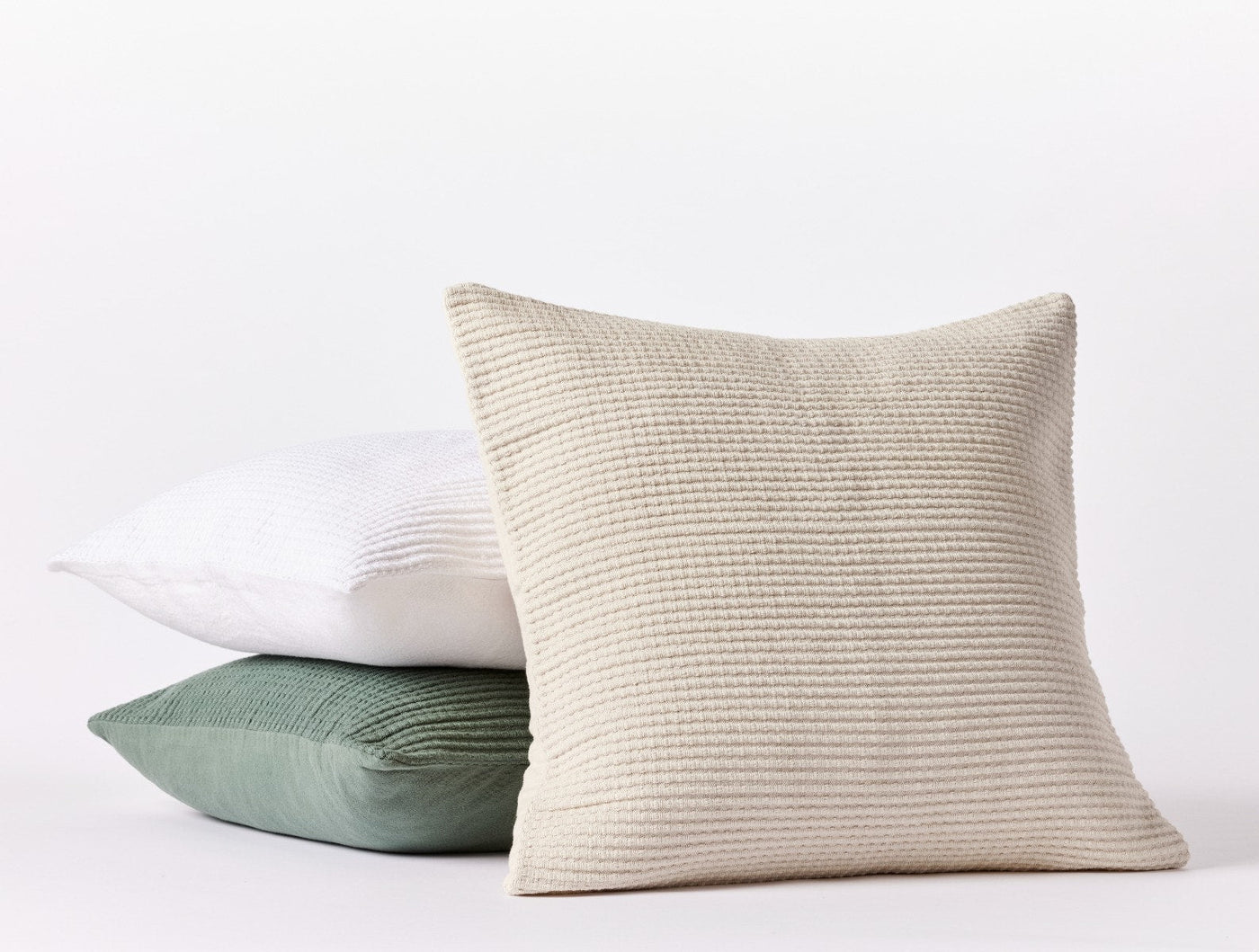 Three stacked Coyuchi Marshall pillow covers in ivory, white, and sage green showing textured weave detail.