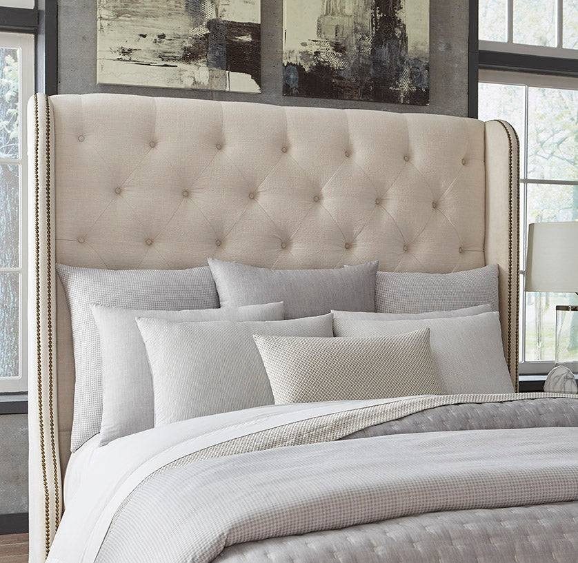 Ivory tufted upholstered wingback headboard styled with layered pearl and grey bedding.