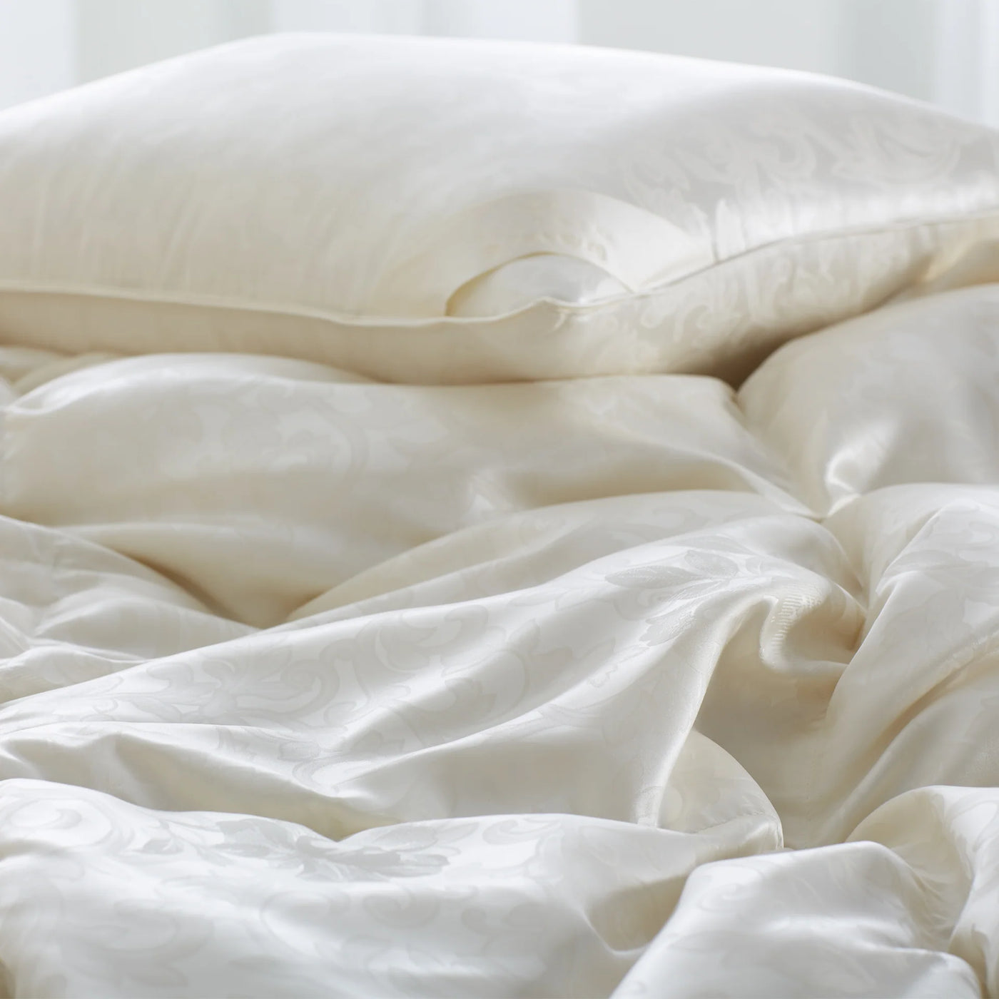 Close-up of ivory silk duvet with lustrous sheen and softly rumpled folds.