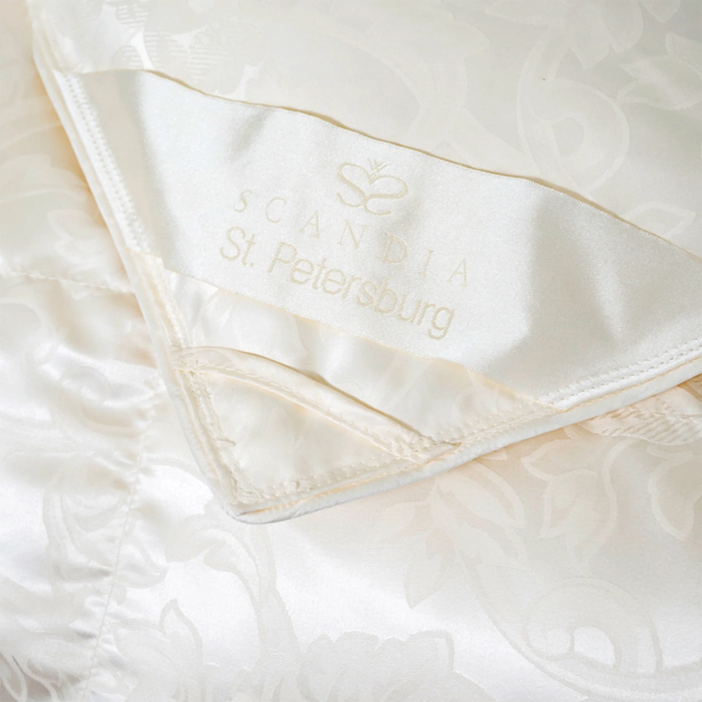 Close-up of ivory satin label with Scandia St. Petersburg branding on floral jacquard duvet.