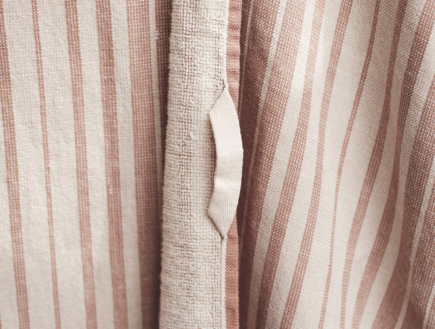 Close-up of duvet tie loop on terracotta-striped cotton linen fabric.