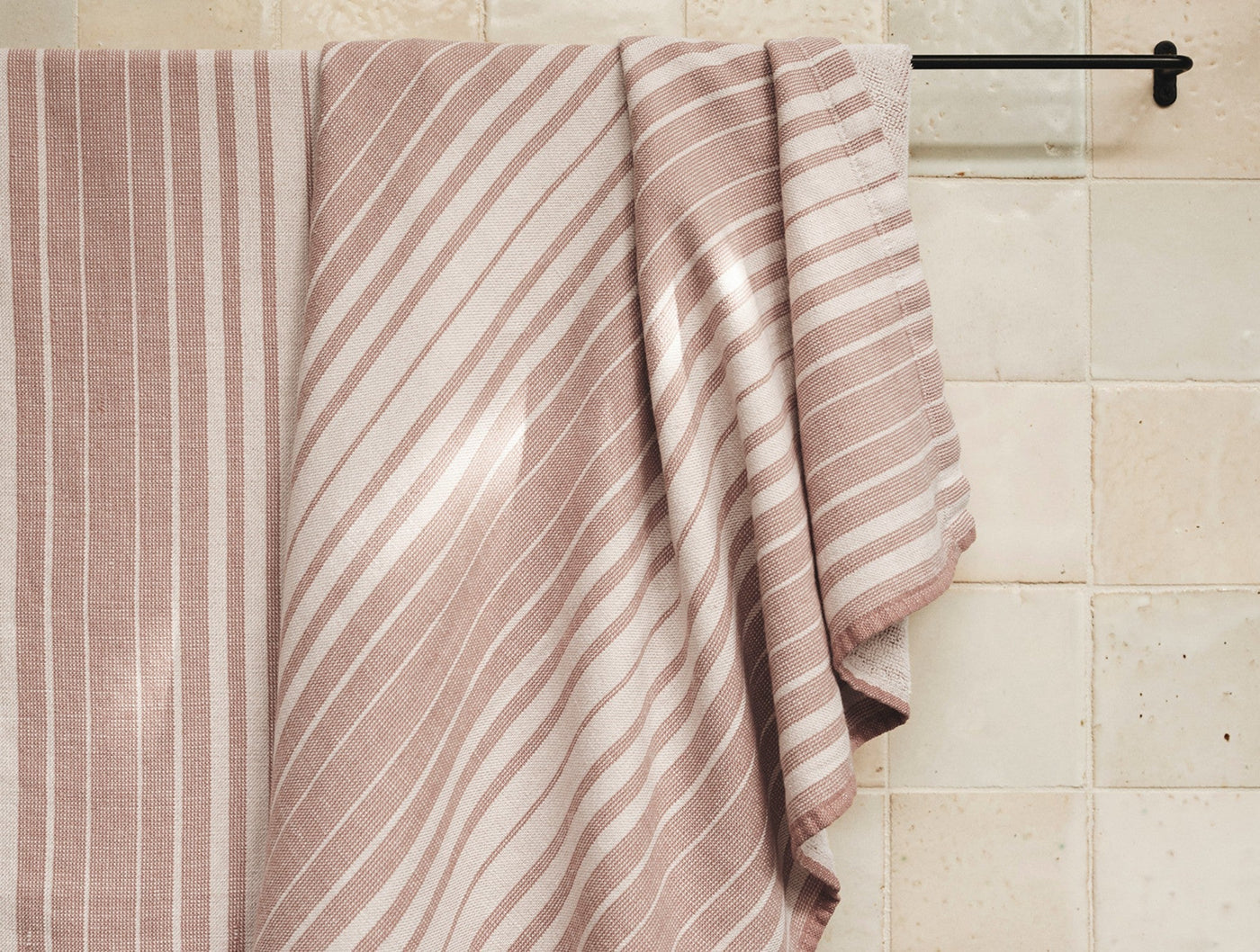 Dusty rose and ivory striped linen cotton bath towels draped over a black towel bar.