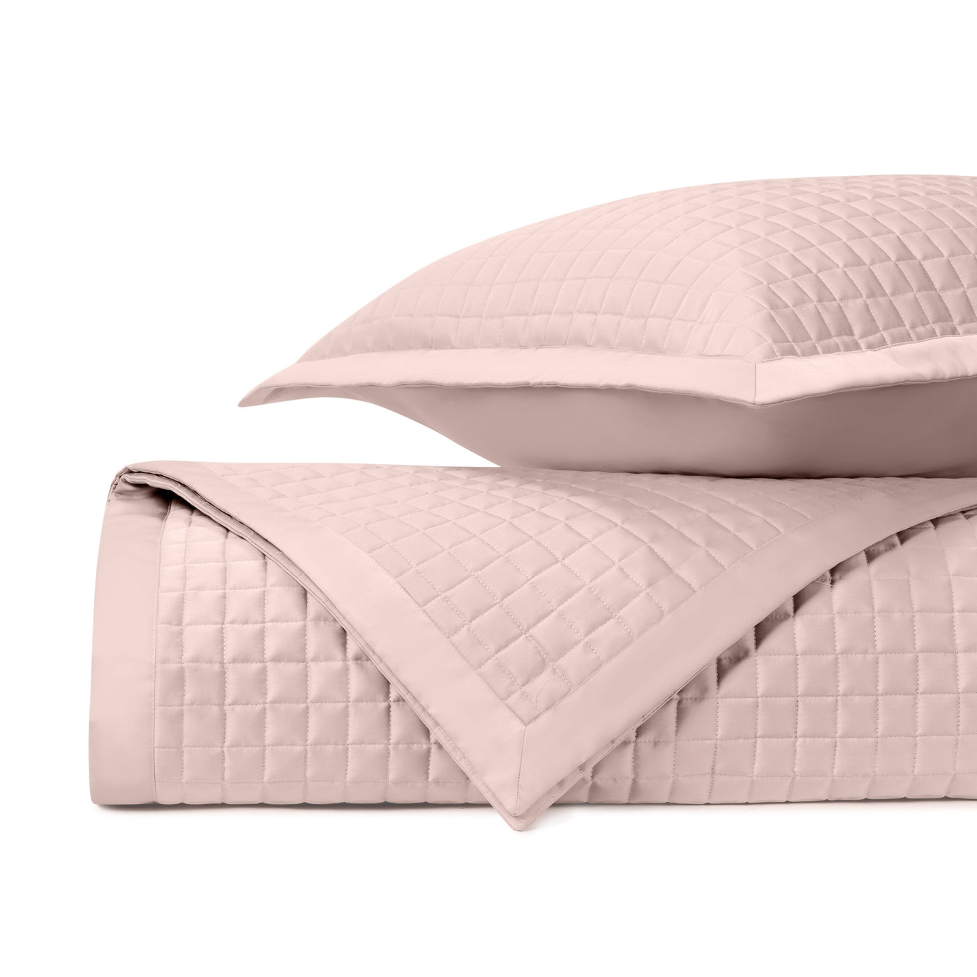 Close-up of blush quilted fabric with grid stitching pattern, folded with matching sham.