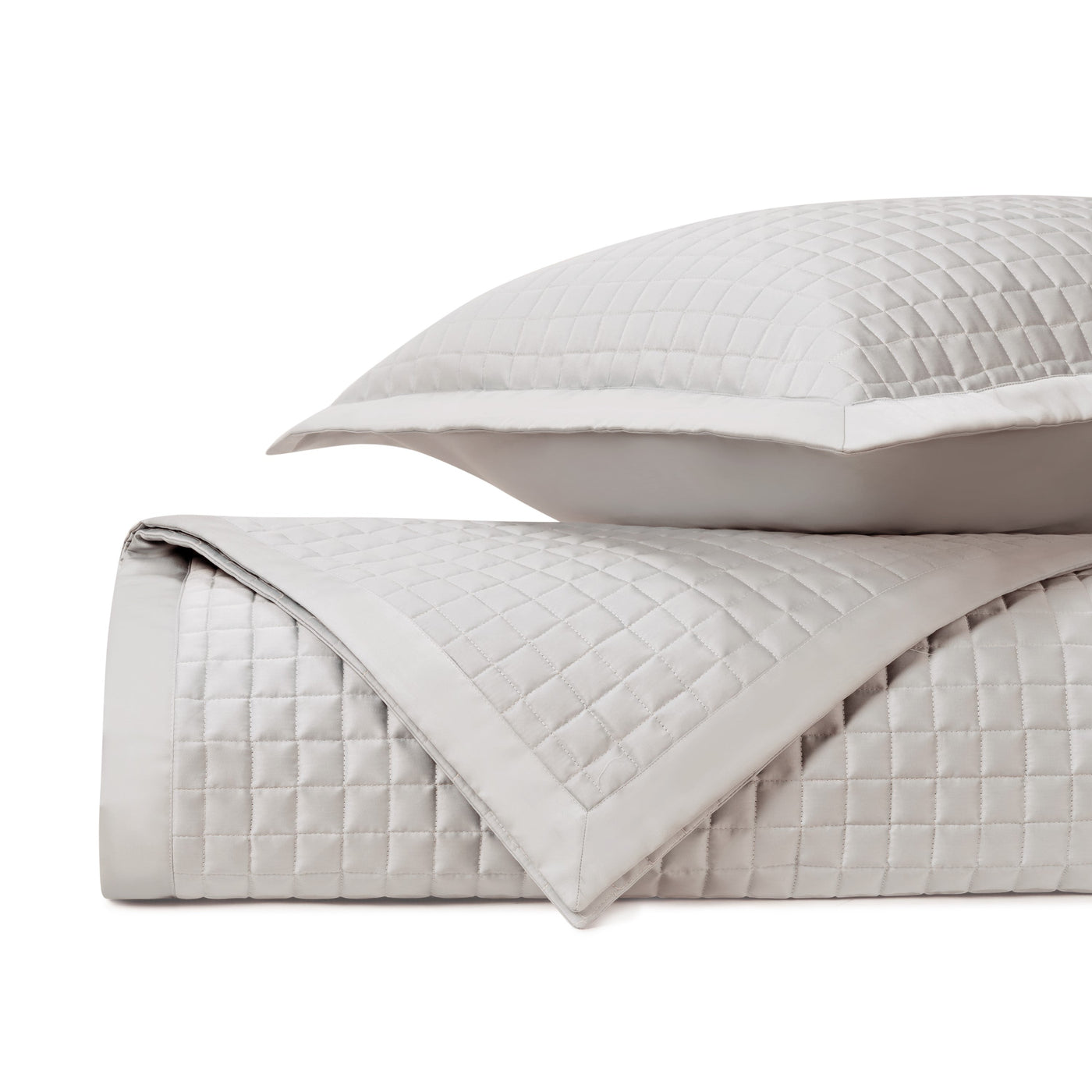 Close-up of pearl quilted coverlet folded with matching sham, square grid stitching detail.