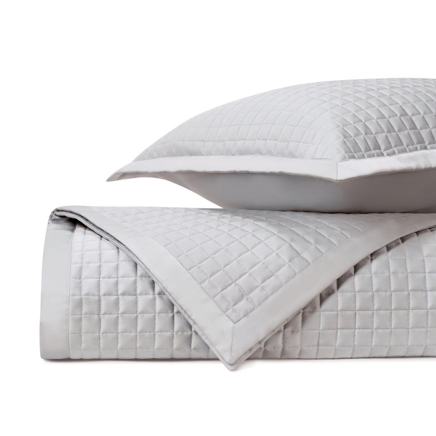 Close-up of silver quilted coverlet and sham showing square stitching pattern and border detail.
