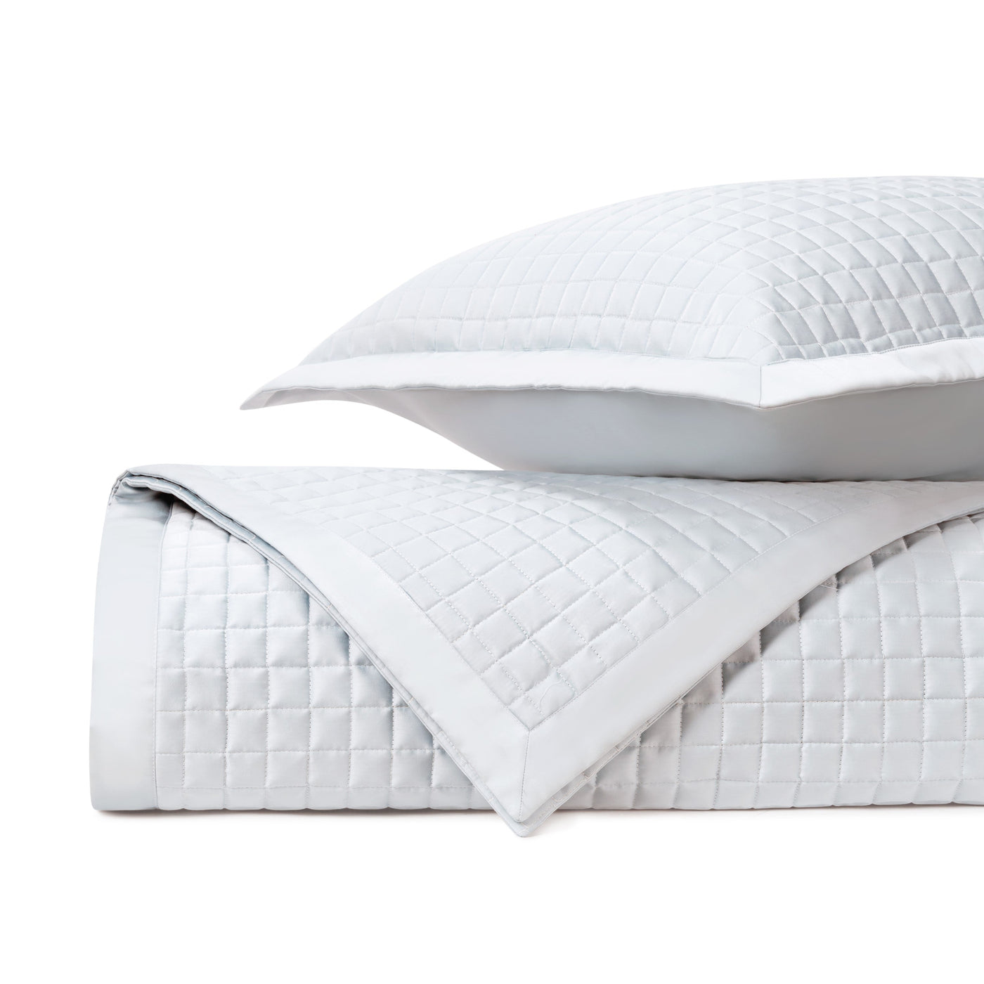 Close-up of white quilted coverlet and sham with square stitching pattern, folded and stacked.