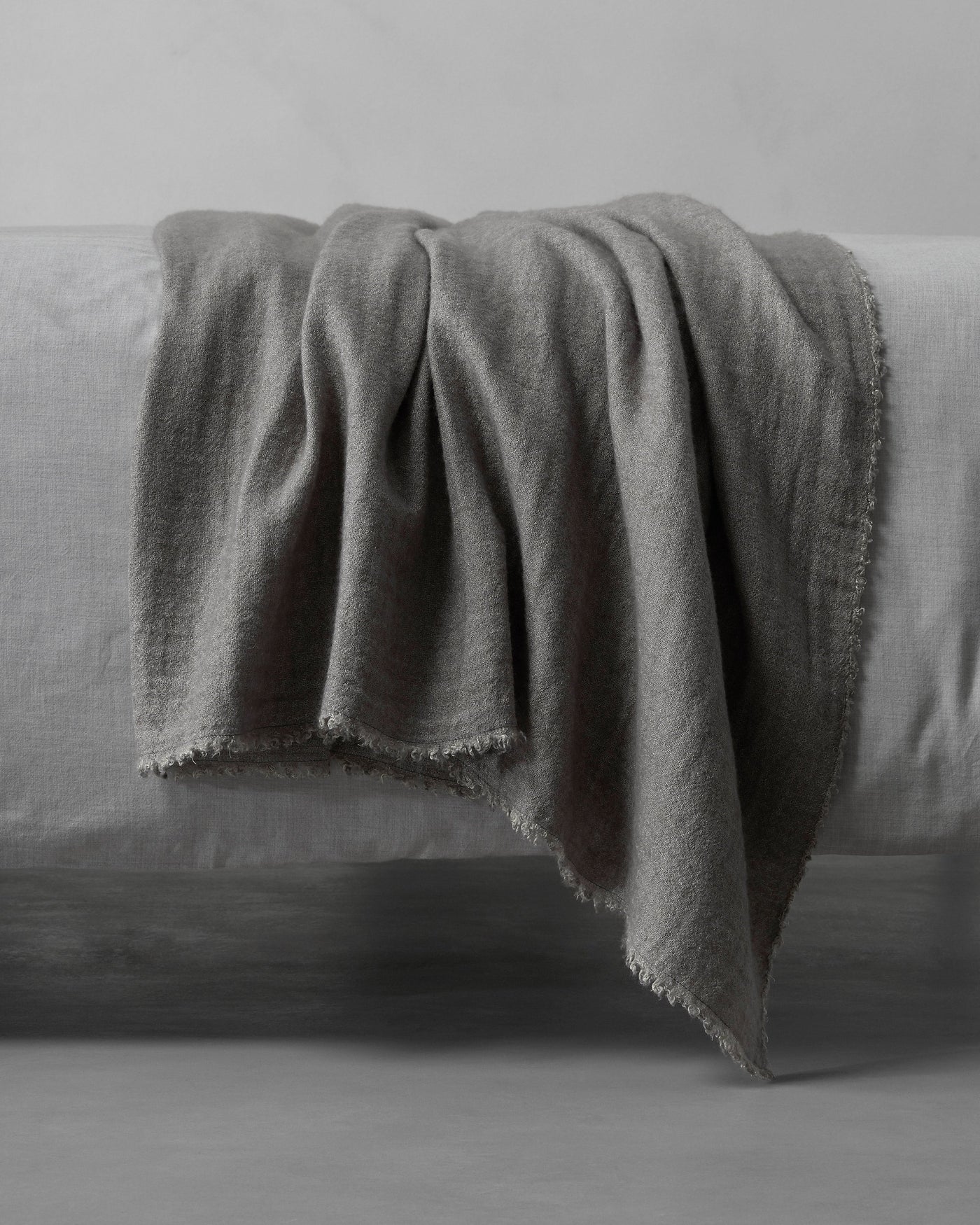 Society Limonta Tiub throw in slate grey draped over a linen bed, showing frayed edge detail.