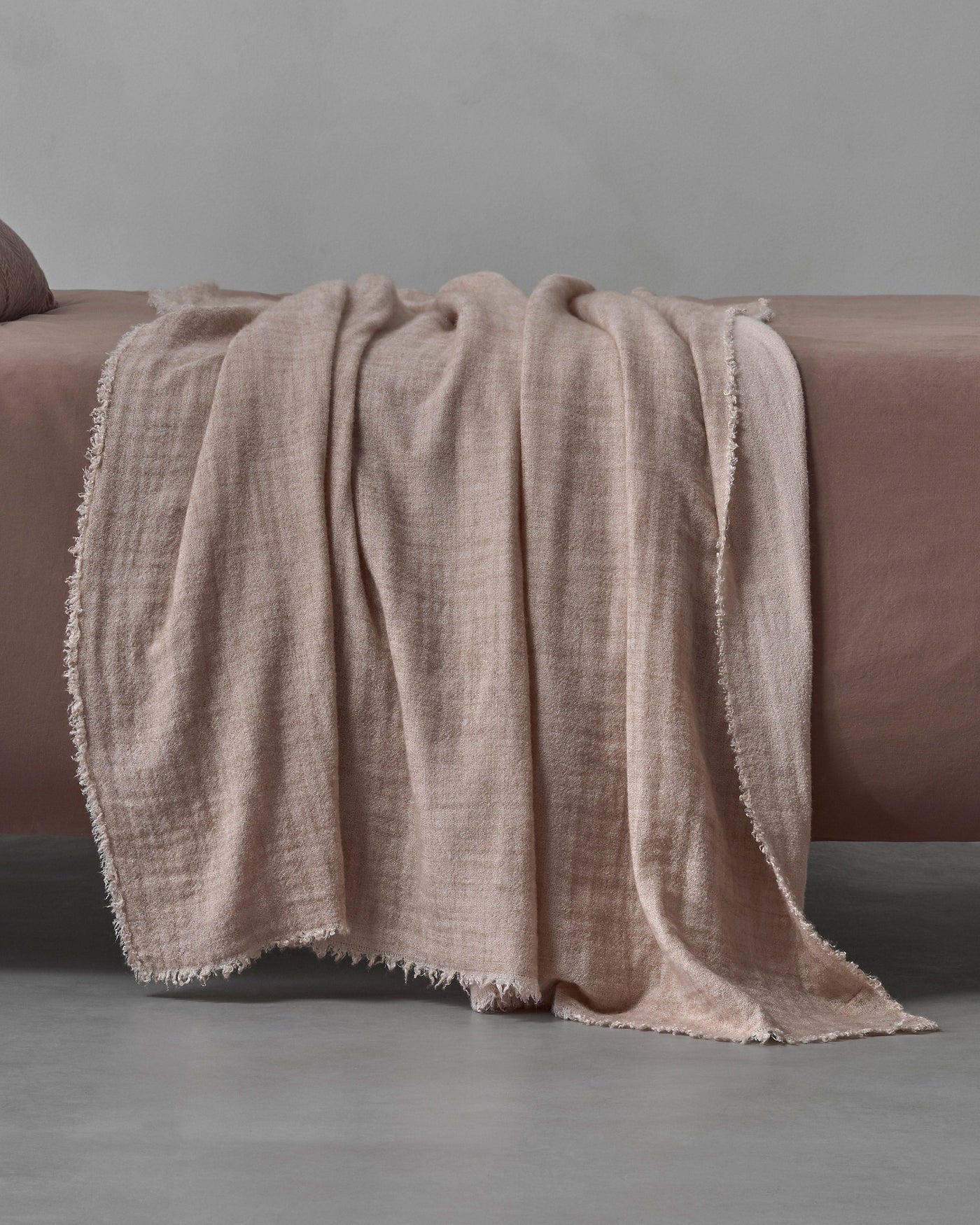 Society Limonta Tiub throw in blush, draped over a bed showing frayed edges.