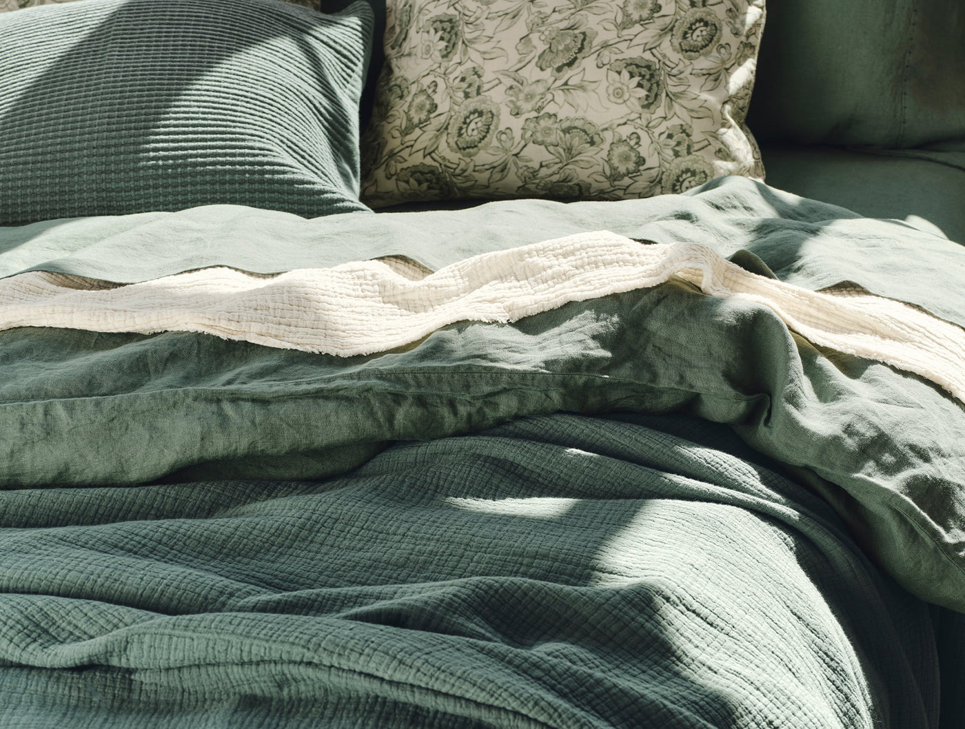 Close-up of Coyuchi Topanga Matelassé blanket in sage, layered with linen duvet in sunlight.