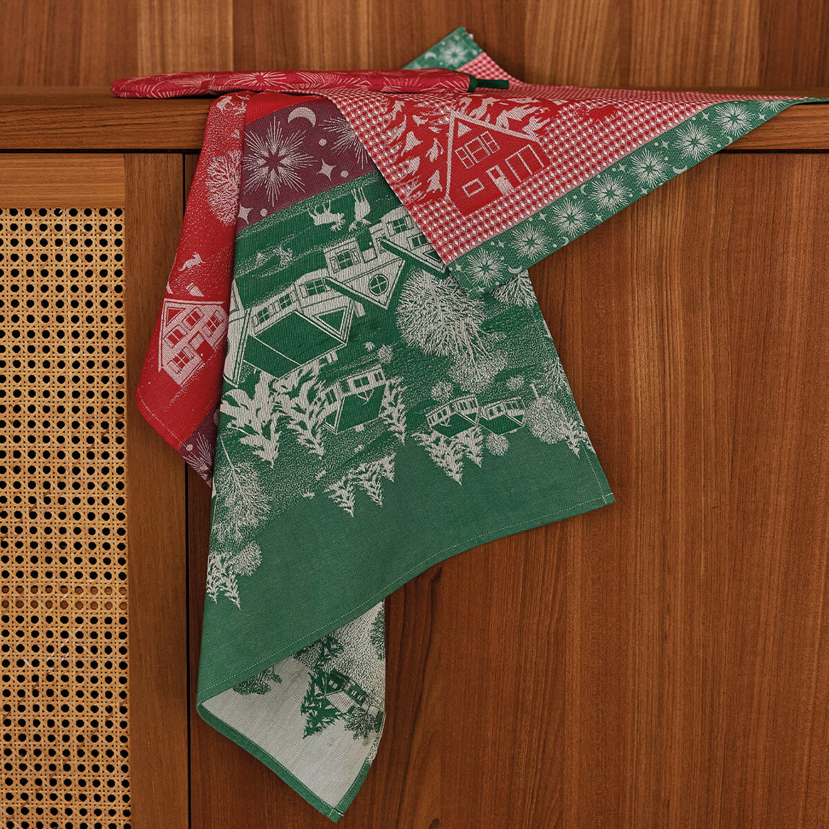 Le Jacquard Français Sous les Étoiles tea towels draped over cabinet, red and green holiday jacquard pattern.