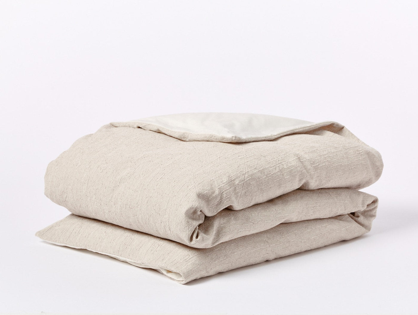 Folded oatmeal linen duvet cover showing natural texture and ivory interior contrast.