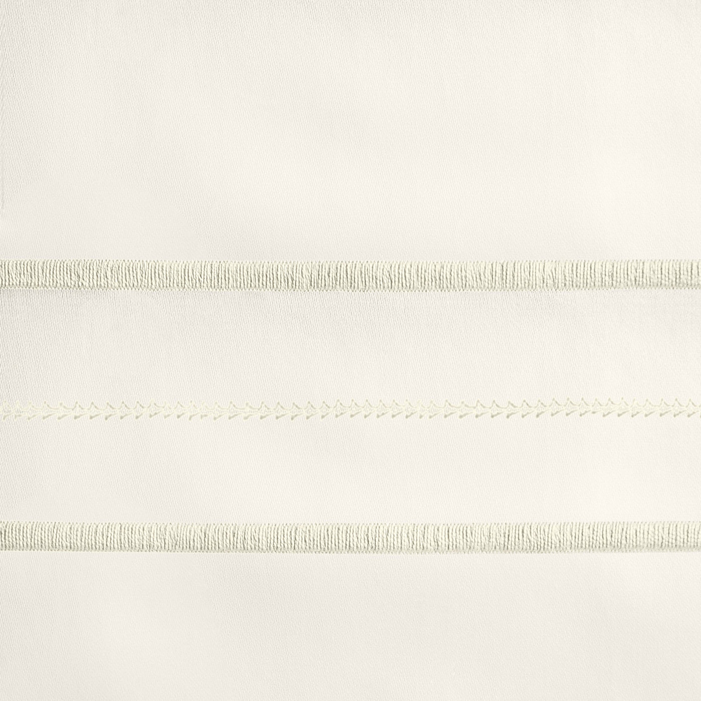 Close-up of ivory embroidered trim with fringe and chevron stitch detailing.