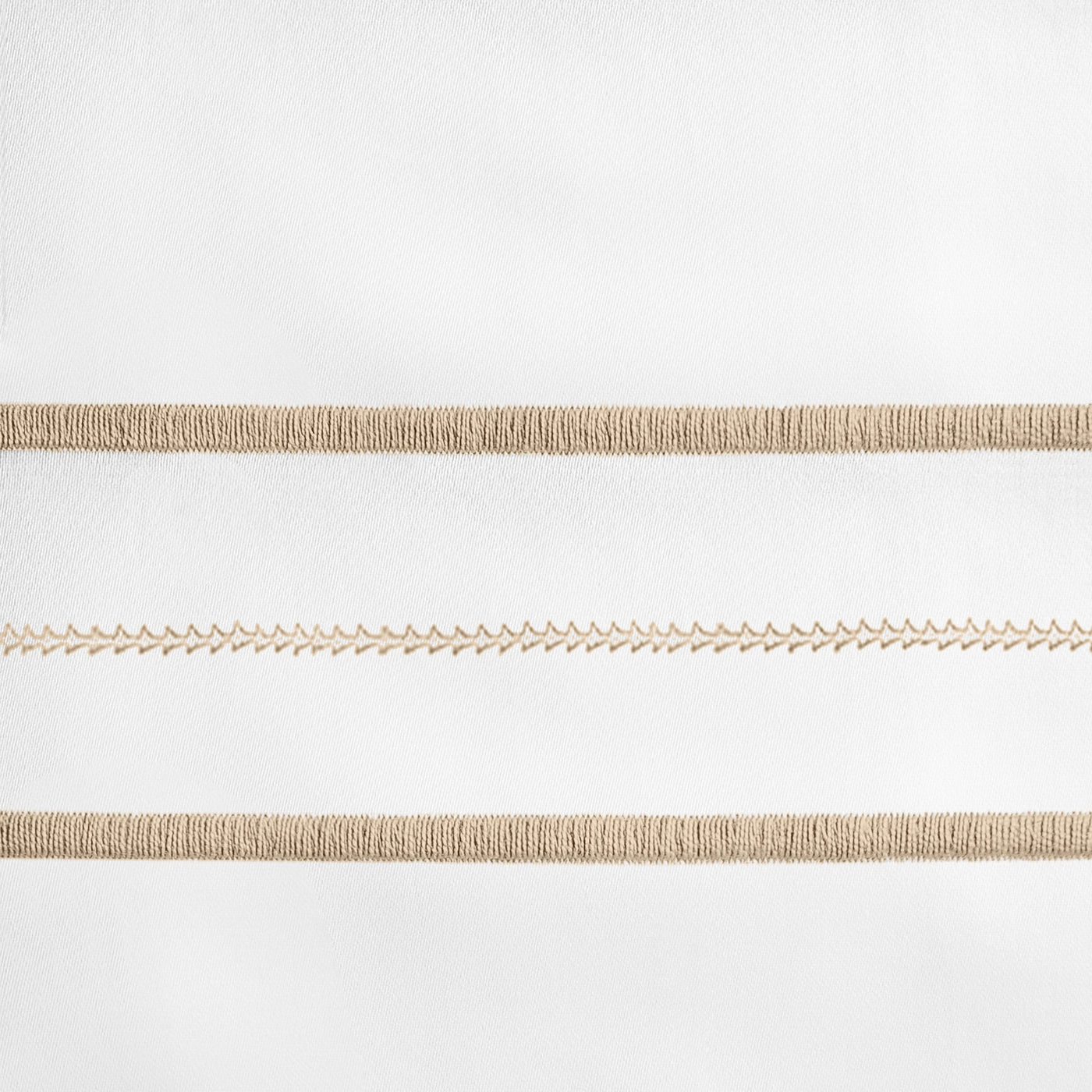 Close-up of champagne embroidered stripe detail on white linen pillowcase.