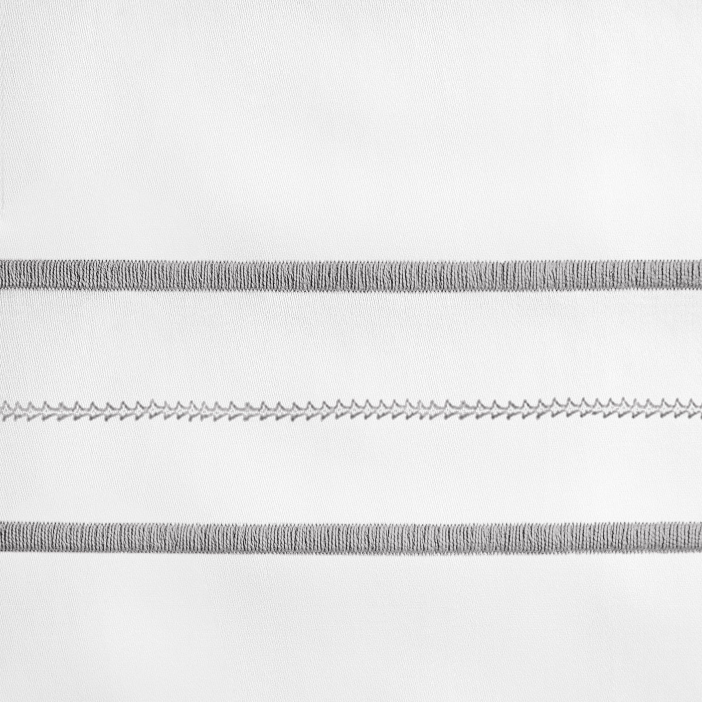Close-up of grey embroidered stripe detail on white linen fabric.