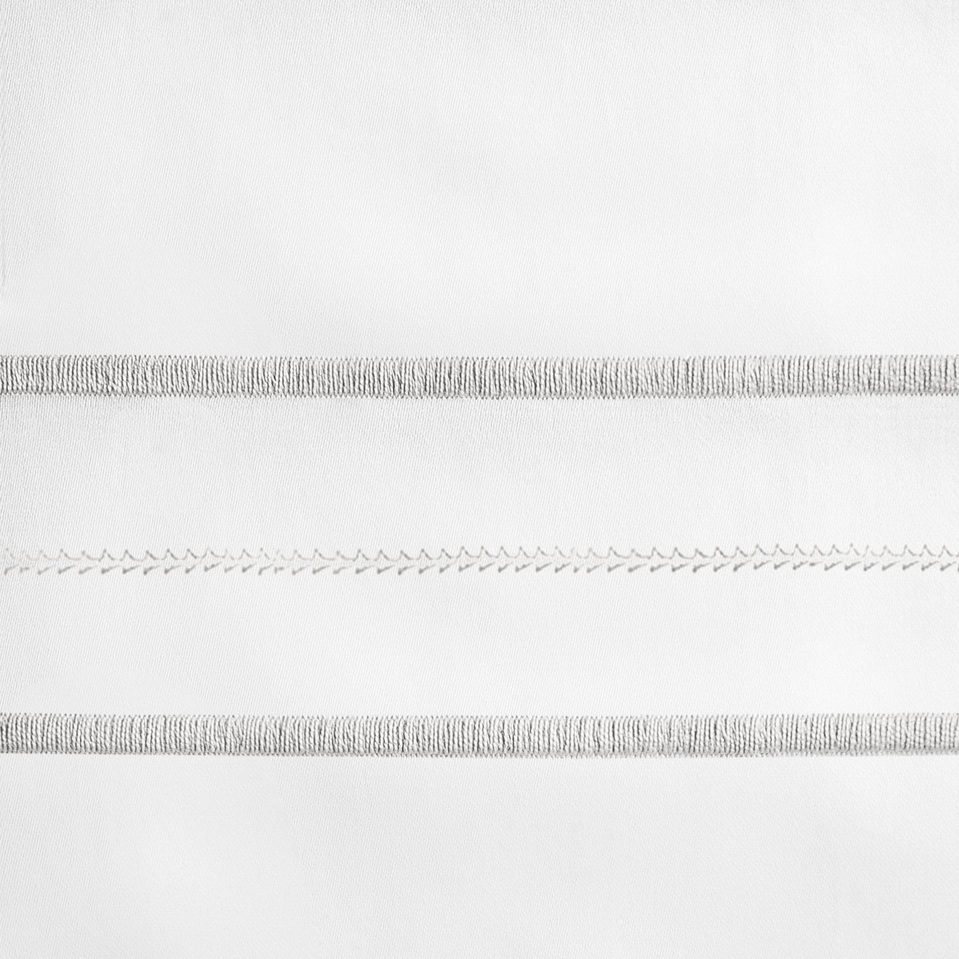 Close-up of Triad embroidery detail showing silver stitch bands on white linen.