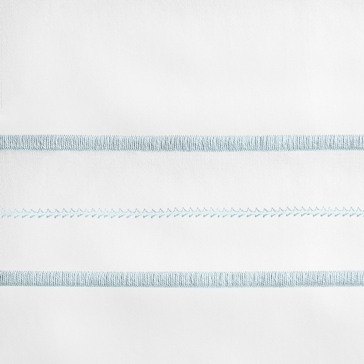 Close-up of sky blue embroidered stripe details on white linen pillow sham.