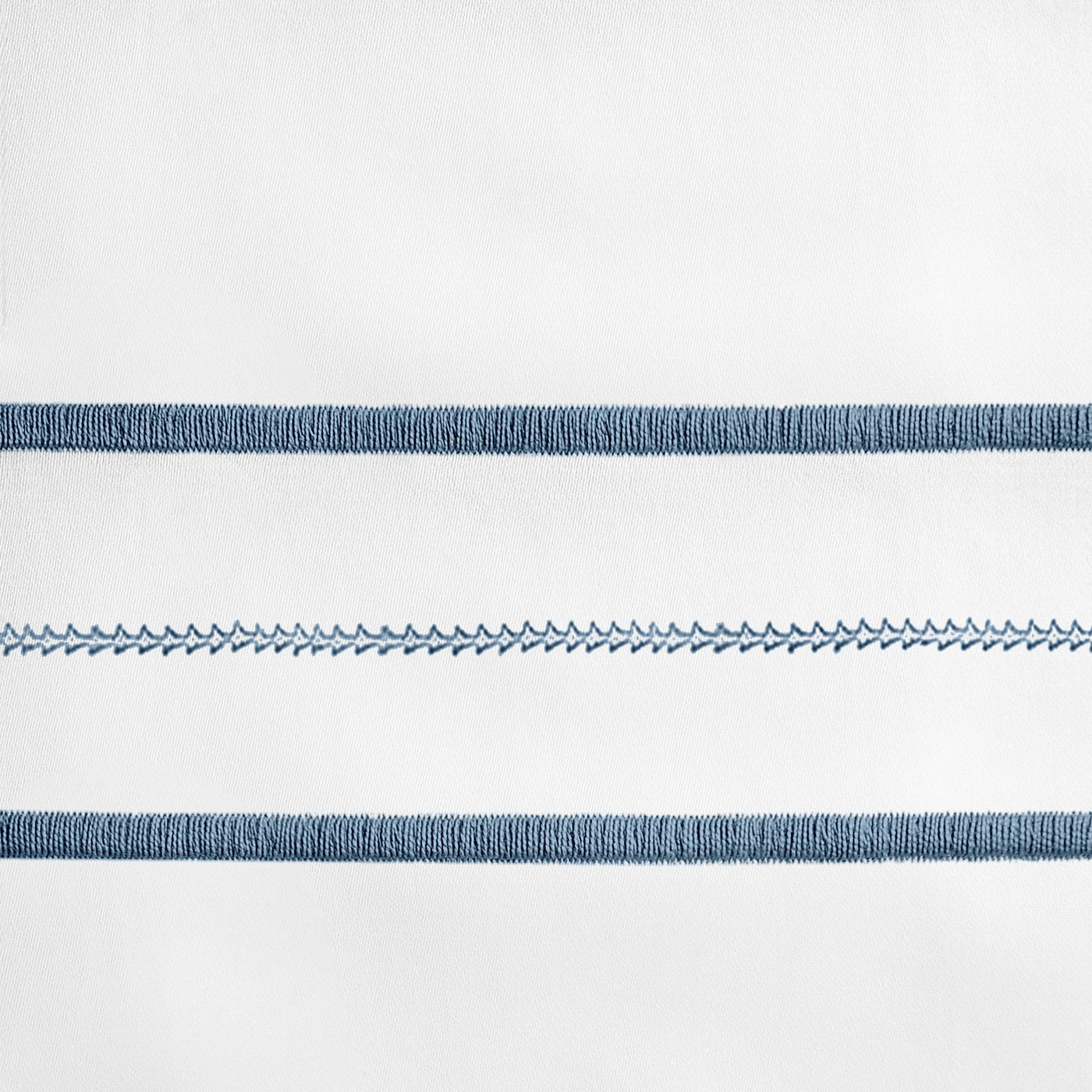 Close-up of steel blue embroidered stripe detail on white linen pillowcase.