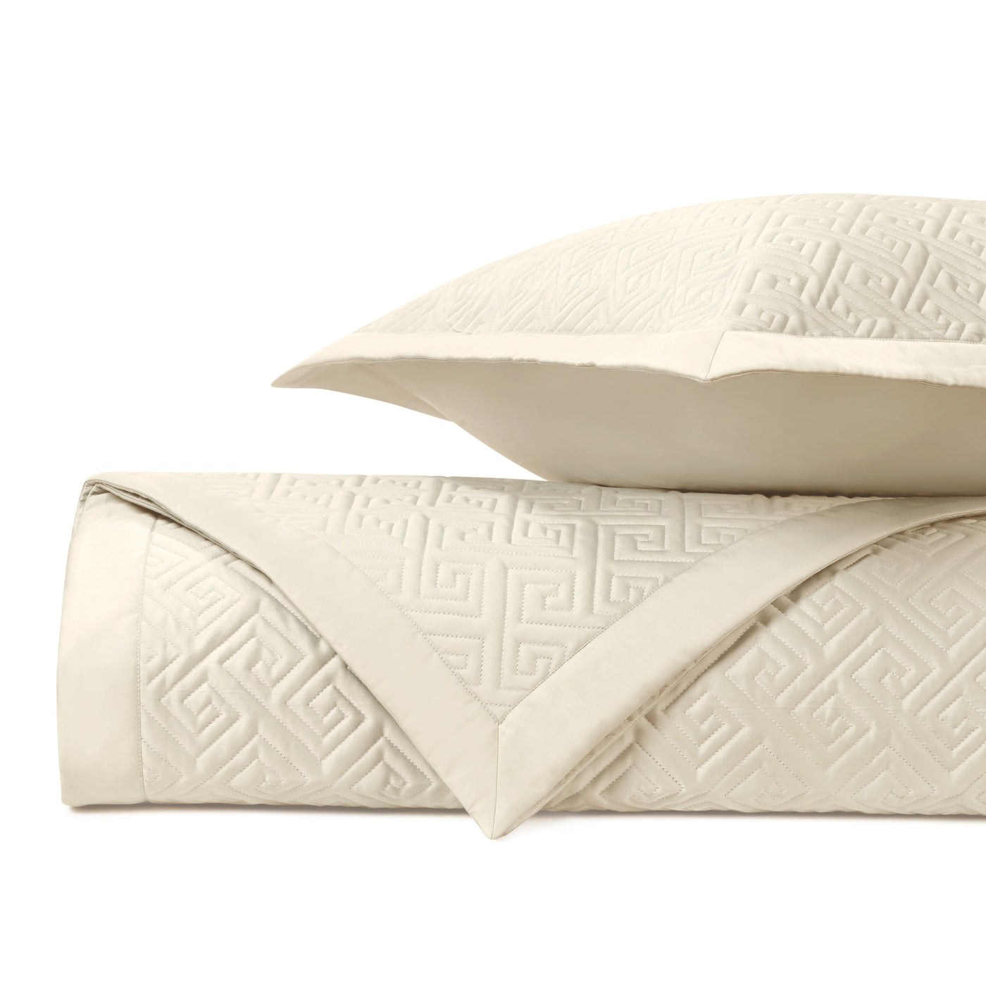 Close-up of ivory quilted coverlet with tone-on-tone Greek key pattern, folded with matching sham.
