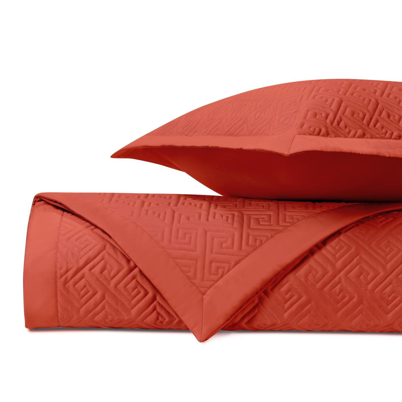 Folded terracotta quilted coverlet and sham showing embossed Greek key pattern detail.