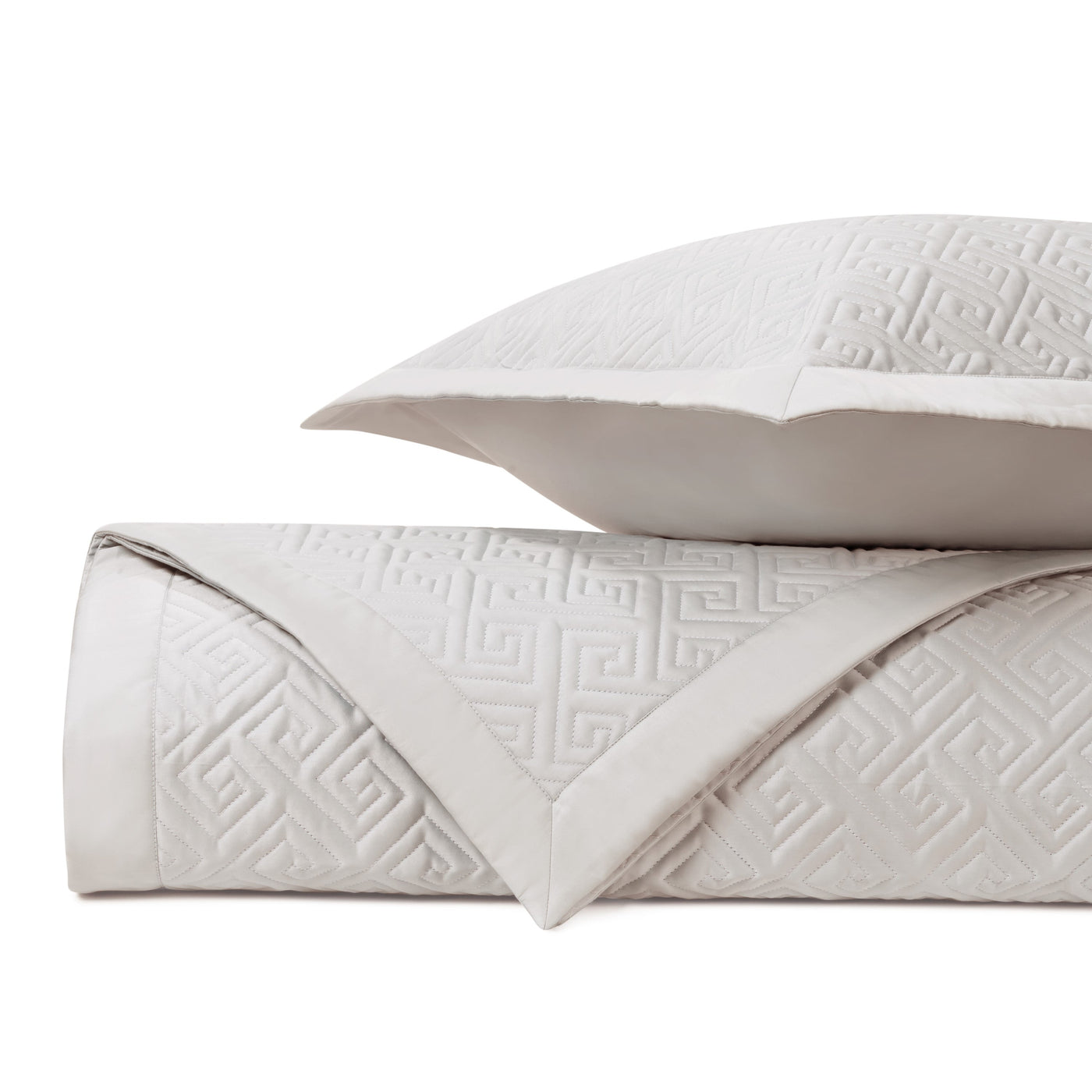 Close-up of ivory quilted coverlet with Greek key pattern, folded with matching euro sham.