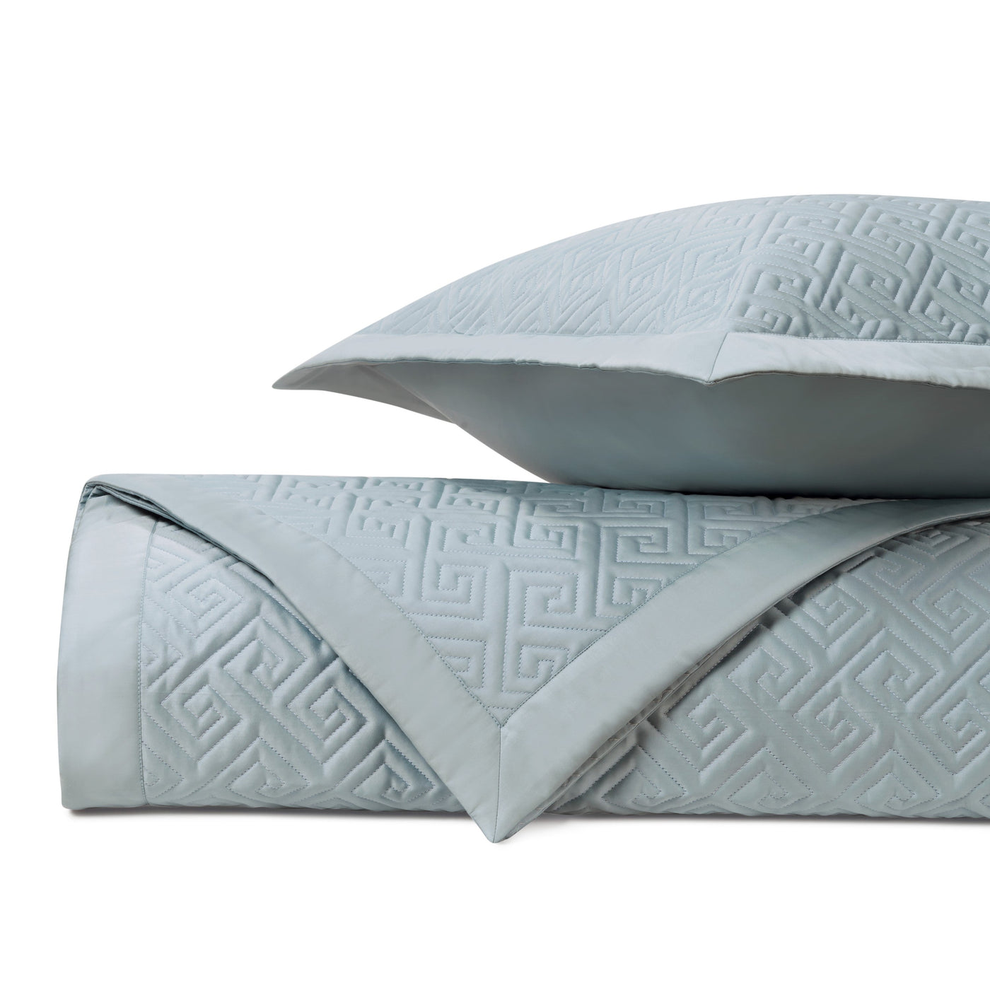 Close-up of mist blue quilted coverlet folded with sham, Greek key embossed pattern.