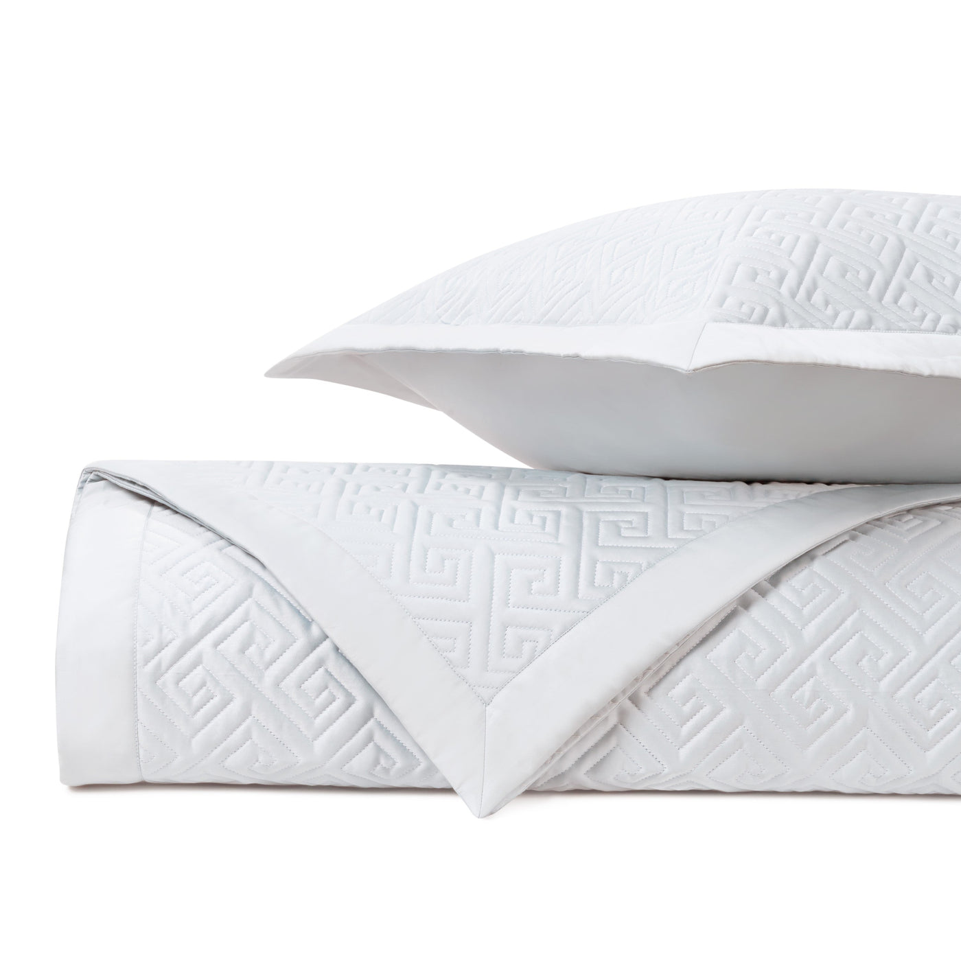Close-up of white quilted coverlet with geometric Greek key pattern and satin border trim.