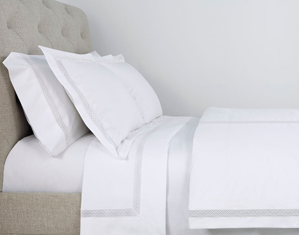 Close-up of Valencia silver Greek key embroidery detail on white cotton bedding.